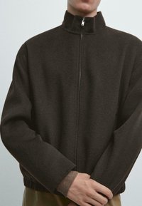 Ciemnobrązowa kurtka na zamek z wysokim kołnierzem, wykonana z miękkiego materiału. Posiada boczne kieszenie i elastyczne mankiety z fakturowaną podszewką.