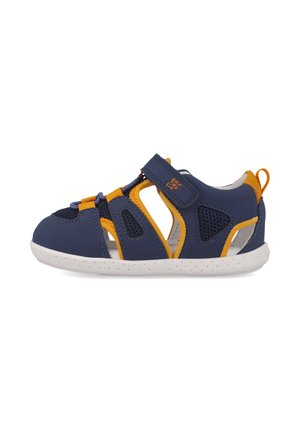 Sandalias azul marino con acentos amarillos, hechas de material sintético, con diseños troquelados, una correa de velcro y una suela blanca.