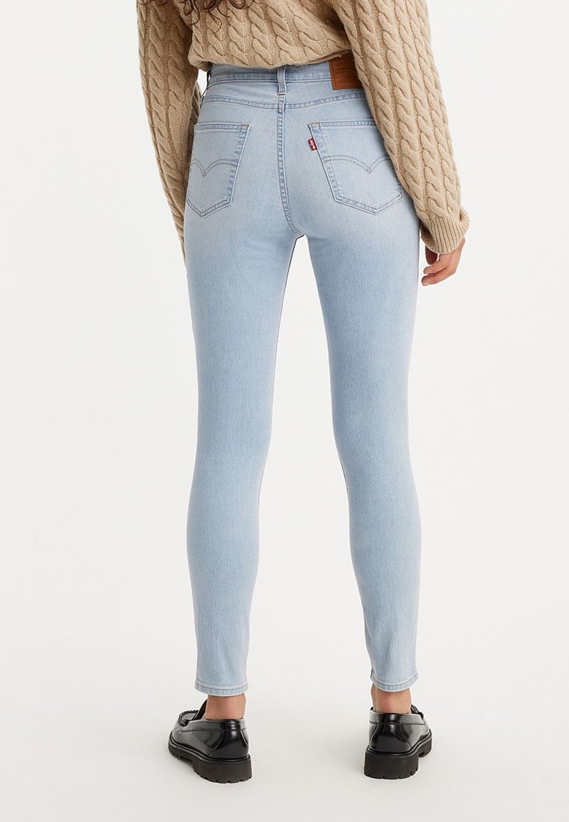Jean skinny bleu clair en denim, avec une taille haute, des poches arrière et une étiquette en cuir marron avec logo sur la ceinture.