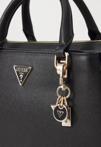 Sac en cuir noir texturé avec des accessoires en or, présentant un logo triangulaire et des charm's, des poignées courtes et une fermeture à glissière.