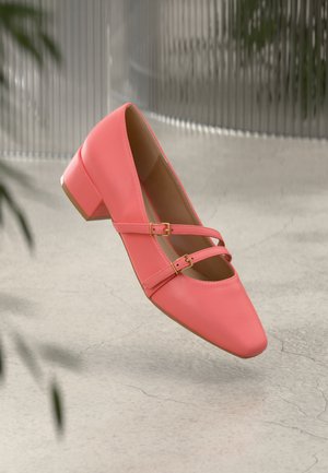 Coral leather low-heeled shoe with a pointed toe, featuring dual straps and gold-tone buckles. Smooth texture, minimalistic design.