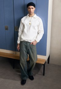 Bílá bavlněná mikina s límečkem a žebrovanými manžetami, v kombinaci se světle modrými džíny. Černé tenisky dotvářejí celý outfit.