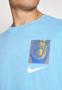 Világoskék pamut póló, kék és sárga színű kosárlabda gyűrű grafikával, az elején fehér Nike logóval.
