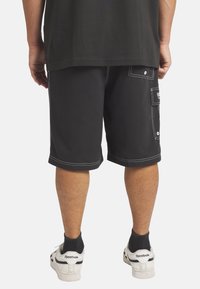 Mustat cargo-shortsit, joissa on valkoiset kontrastitikkaukset, sivutaskut ja suora leikkaus. Yhdistetty valkoisiin lenkkareihin ja mustiin putkilehden sukkiin.