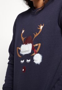 Sudadera azul marino con un diseño de reno con astas marrones, sombreros de piel sintética blanca, un gorro de Santa brillante rojo y detalles negros en las pestañas.