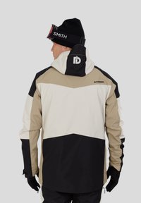 Pánská nepromokavá bunda v béžové, černé a bílé barvě. Má kapuci, elastické manžety a černé rukavice. Hladký materiál s označenými detaily.