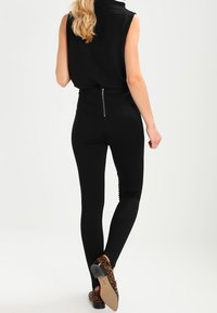 Svarta leggings med en figurnära design och slät textur, med en bakre dragkedjedetalj, ihop med skor med djurmönster.