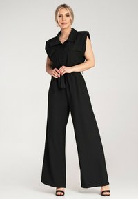 Czarny kombinezon z krótkimi rękawami, zapinany na guziki z przodu i szerokimi nogawkami. Posiada dwie kieszenie na piersi oraz paskiem w talii, co podkreśla sylwetkę.