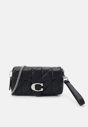 Pochette en cuir matelassé noir avec une chaîne argentée, une grande boucle "C" en argent et une sangle de poignet amovible sur fond blanc.