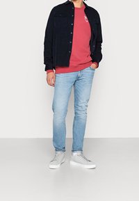 Navy button-up shirt over a red sweatshirt, light blue jeans, and grey sneakers. Shirt features two pockets and a casual fit.