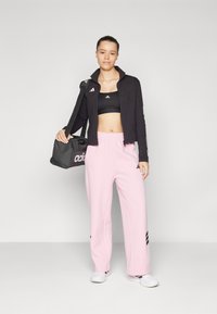 Črna jopica na zadrgo, črn športni modrček, roza trenirke, bele čevlje in črna torba z logotipom "adidas". Značilnosti vključujejo črte na jopici in hla�čah.