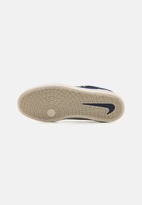 Zilā sporta apavu zole ar strukturētu gumijas virsmu, kurā ir zigzaga raksts un melns Nike swoosh. Gaiši krāsoti malas uzlabo kontrastu.