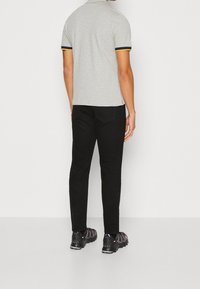 Polo grigio con bordi neri e gialli, abbinato a pantaloni neri e sneakers nere, visto da dietro.