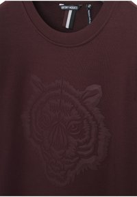Camiseta burdeos con un diseño texturizado de cabeza de tigre, fabricada en algodón suave, con cuello redondo y una etiqueta con rayas en blanco y negro.