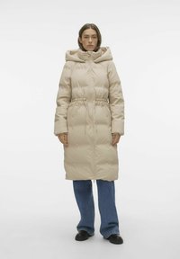 Manteau matelassé beige avec cordon de serrage à la taille, capuche oversize et fermeture éclair à l'avant. Il dispose de longues manches et d'un tissu lisse, légèrement brillant.