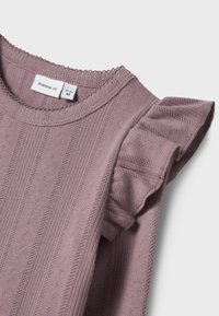 Liliowy sweter z dzianiny z prążkowanym wykończeniem, drobnymi zdobieniami oraz falbanami na ramieniu. Metka mówi "name it."