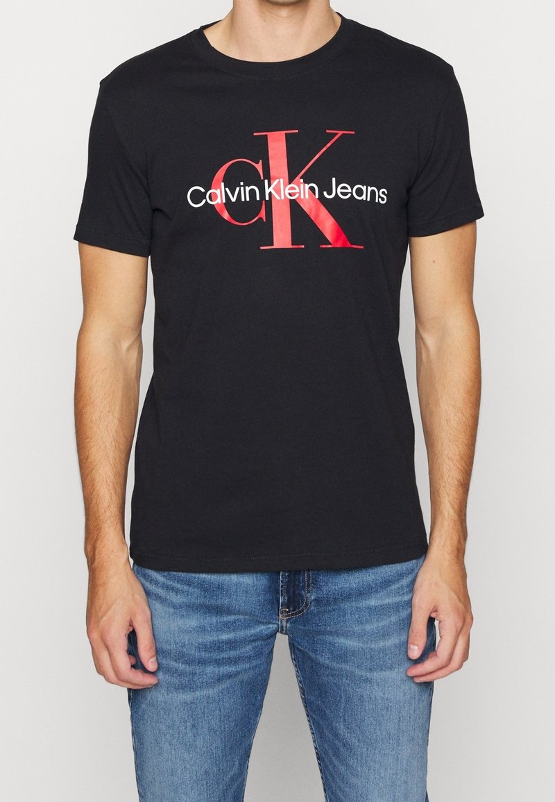 Svart bomulls t-shirt med en framträdande röd "CK" logo och "Calvin Klein Jeans" tryckt nedan i vitt. Korta ärmar och rund hals.