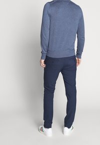 Chino blu navy e un maglione blu, con colletto e polsini a coste. L'outfit è abbinato a sneakers bianche con accenti verde, rosso e nero.