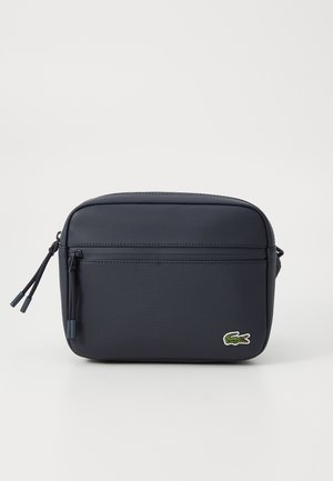 Navy blue rectangular shoulder bag made of textured synthetic material, featuring a front zip pocket and a green Lacoste logo.