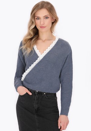 Cardigan tricotat albastru cu o dantelă albă ondulată pe de-a lungul gulerului, asortat cu o fustă din denim negru. Mâneci lungi și material texturat.