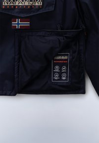 Chaqueta navy con bolsillo de malla, parche de la bandera de Noruega y dos etiquetas de tela que indican materiales resistentes al agua, a prueba de viento y transpirables.