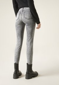 Jeans de mezclilla delgada en gris con una textura desgastada, dos bolsillos traseros y cintura a media altura, combinados con botas negras hasta el tobillo con suelas gruesas.