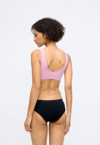 Verstelbare roze sportbh met een V-vormige achterkant, gecombineerd met zwart hoge taille slip met kanten rand langs de taille.
