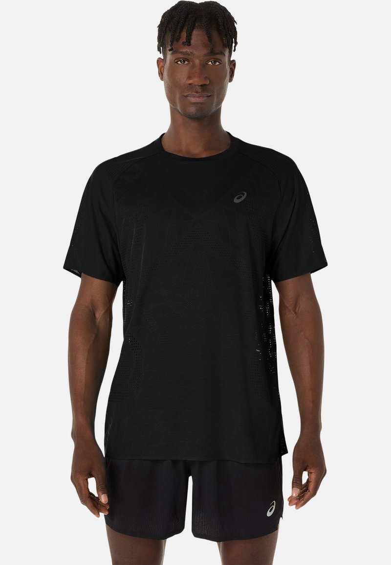 Schwarzere sportliche T-Shirt mit kurzen Ärmeln, das ein strukturiertes Stoffmuster und ein reflektierendes Logo auf der linken Brust aufweist. Getragen mit passenden Shorts.
