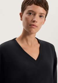 Maglione nero a V con una vestibilità comoda, realizzato in un tessuto morbido e liscio con un colletto a coste. Design pulito, senza motivi o accenti visibili.