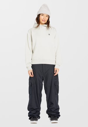 Haut à capuche gris clair avec une poche et un logo, associé à un pantalon cargo noir ample avec des zips et des poches latérales, porté avec des baskets noires.