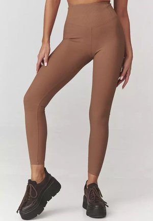 Brązowe prążkowane leginsy o wysokim stanie z teksturowanym wykończeniem, w zestawieniu z ciemnymi platformami. Skupienie na dopasowanej sylwetce.