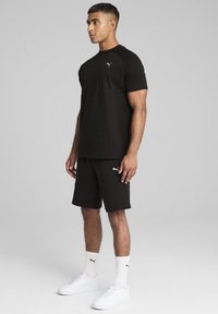 Svart bomullströja med korta ärmar och en vit logotyp på bröstet, kombinerad med svarta shorts och vita sneakers. Enkelt design, inga mönster.