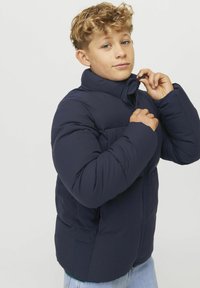 Marineblaue gepolsterte Jacke mit hohem Kragen und Reißverschluss, ausgestattet mit einer glatten Textur und zwei vorderen Taschen.