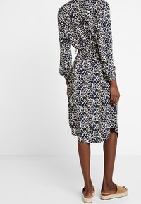 Klänning i leopardmönster med långa ärmar, med ett knyt i midjan, mjukt tyg och en knälång fåll, kompletterad med avslappnade skor att slida på.