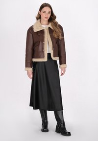 Brun læder cropped jakke med en beige shearling krave og manchetter, parret med en lang sort satin nederdel og sorte ankelstøvler.
