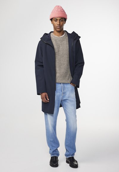 Marinblå vattentät jacka, texturerad grå tröja, ljusblå jeans och svarta skor; kompletterad med en rosa stickad mössa.