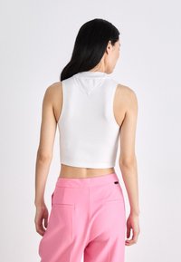 Top corto blanco sin mangas con un cuello alto y una pequeña capucha, combinado con pantalones rosa a medida que cuentan con bolsillos laterales.