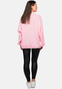 Roze gebreide oversized trui met een gestructureerde afwerking, gecombineerd met zwarte legging en witte sneakers. De trui heeft een losse pasvorm en een geribbelde zoom.