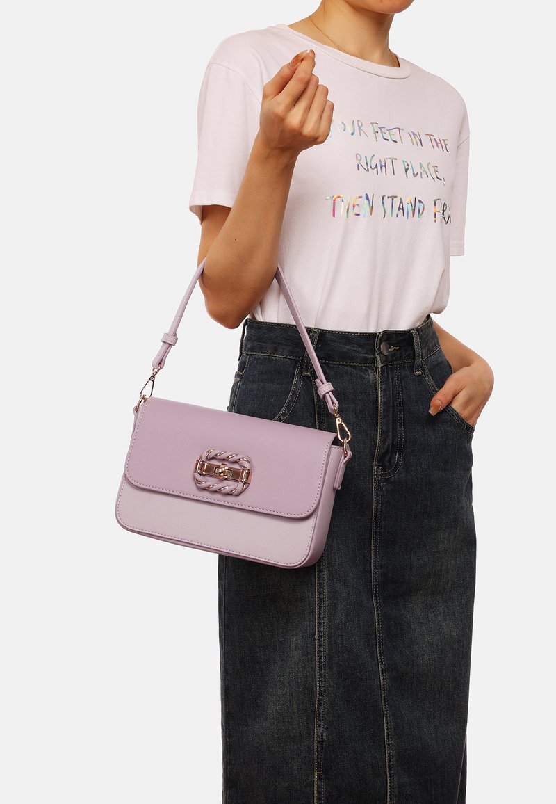 Borsa a tracolla in ecopelle lilla con chiusura a twist-lock, accentata da una treccia e dotata di tracolla rimovibile, abbinata a una maglietta grafica e a una gonna di jeans.