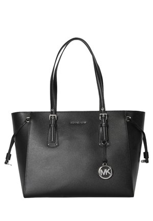 Sac cabas en cuir noir Michael Kors avec doubles poignées, cordons latéraux et un charm rond argenté avec le logo MK suspendu près des poignées.
