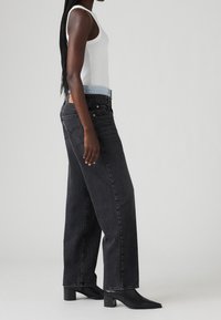 Svarta byxor med vida ben och ett ljusblått midjeband, tillsammans med en vit ribbad linne. Byxorna har en subtil struktur och fem fickor.