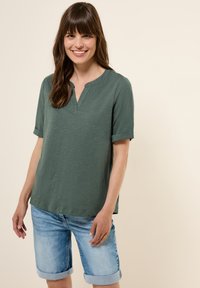 Top verde a maniche corte con scollatura a V, abbinato a pantaloni corti in denim azzurro con risvolto. Tessuto morbido con vestibilità comoda.