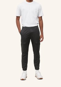 Černé cargo kalhoty s elastickými manžetami, několika postranními kapsami a volným střihem, spárované s bílým tričkem s crew neck a bílými teniskami.