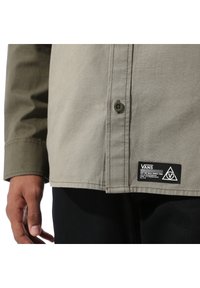 Grijze button-up overhemd van een katoenmix, met een zak met een Vans logo label. Lange mouwen met een getailleerde pasvorm.
