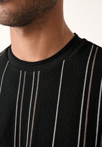 Schwarzes, geripptes T-Shirt mit horizontalen Streifen in Weiß und Hellbraun, mit Rundhalsausschnitt und glatter Textur. Nahaufnahme der Stoffdetails.