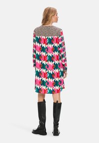 Bunt gemustertes Kleid mit geometrischen Formen in Pink, Grün und Weiß; Yoke im Leopardenmuster; kombiniert mit schwarzen, kniehohen Stiefeln.