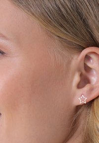 Boucles d'oreilles en étoile en or rose avec un design minimaliste, placées dans une oreille percée. Texture lisse, mettant en valeur une forme géométrique simple.