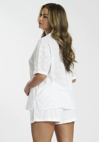 Witte katoenen top met korte mouwen en gaatjesontwerp, met een losse pasvorm, zijsplitten en bijpassende witte shorts, zij-aan-zij weergegeven.