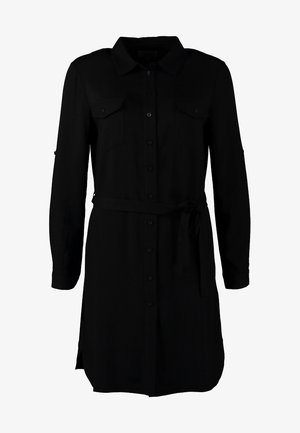 Vestido camisa negro con mangas largas, cinturón en la cintura y dos bolsillos en el pecho. Combinado con botines negros con tachuelas y un sombrero beige.