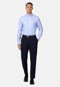  lichtblauw gestreept overhemd met een puntige kraag, knoopsluiting aan de voorkant en lange mouwen, gecombineerd met donkerblauwe broek en zwarte schoenen.